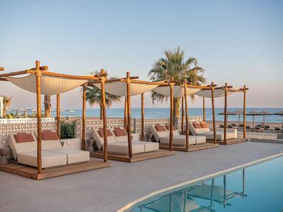 Lits de jour luxueux au bord de la piscine avec vue sur la mer et les palmiers au coucher du soleil.