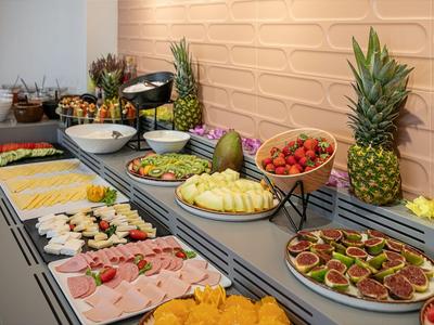 Buffet avec divers fruits, charcuteries et salades devant un mur de pierre clair dans un hôtel.