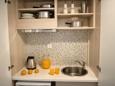 Piccola cucina con lavandino, bollitore, succo d'arancia e bicchieri in un armadio aperto