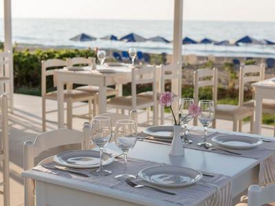 Tavolo apparecchiato con sedie bianche su terrazza con vista sulla spiaggia e sul mare.
