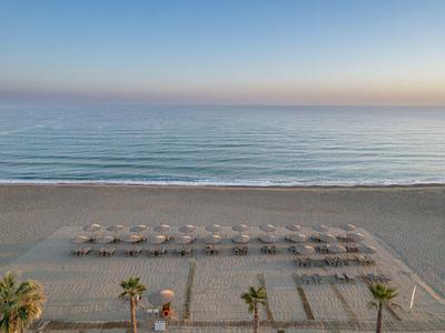 Une plage de sable calme avec des rangées de parasols et des palmiers au premier plan au lever du soleil.