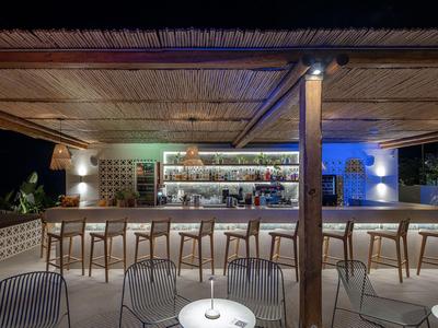 Bar moderno de hotel con techo de madera, barra y filas de taburetes por la noche.