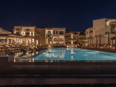 Piscina dell'hotel di notte con lettini illuminati e edifici sullo sfondo