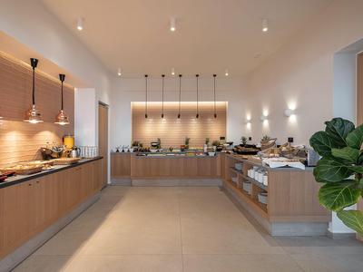 Area buffet moderna con banconi in legno, lampade sospese e piatti apparecchiati in una stanza luminosa.