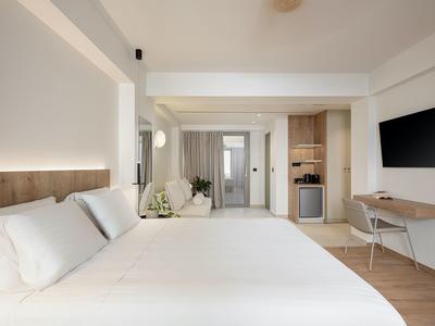 Chambre d'hôtel moderne avec grand lit, bureau, télévision et kitchenette ouverte.