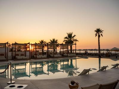 Piscine d'hôtel avec chaises longues et palmiers au coucher du soleil.