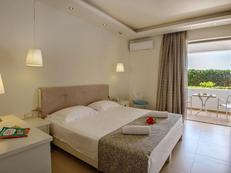 Chambre lumineuse avec lit double et vue sur balcon avec table et chaises.