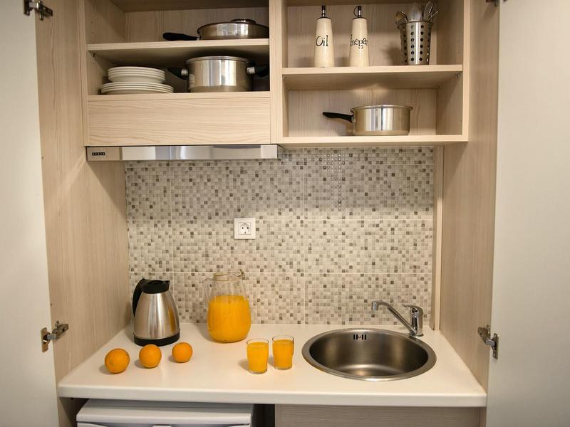 Petit placard de cuisine avec évier, bouilloire, jus d'orange et verres.