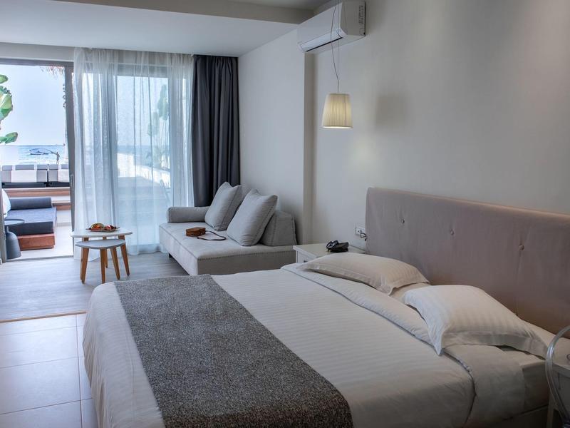 Chambre d'hôtel lumineuse avec lit, coin salon et balcon donnant sur la mer.