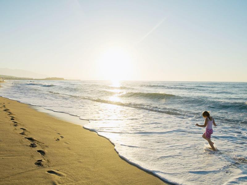 Un enfant joue dans l'eau peu profonde à la plage au coucher du soleil.