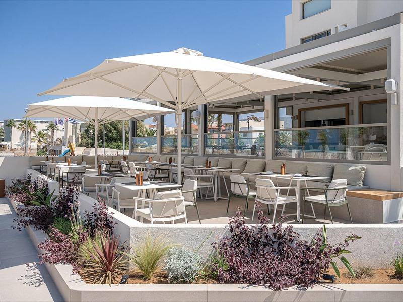 Espace extérieur moderne d'un hôtel avec tables, chaises et grands parasols sous un ciel clair.
