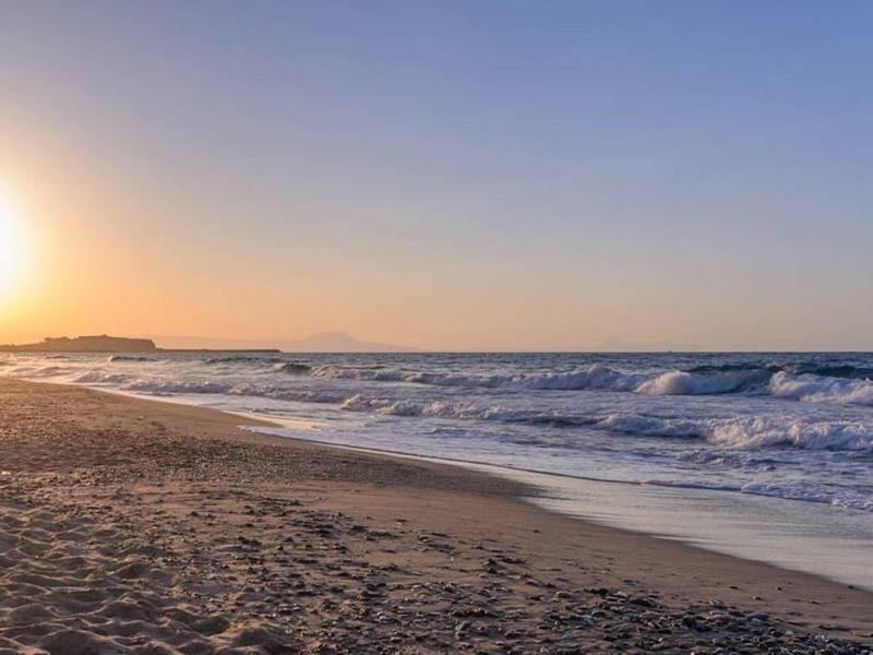 Coucher de soleil sur la plage avec des vagues douces et un ciel clair.