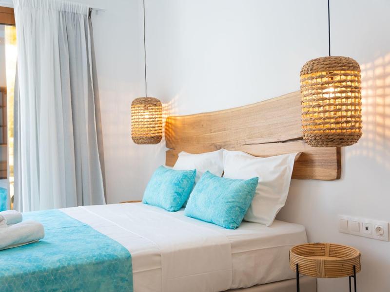 Modern hotelkamer met wit beddengoed, turquoise kussens en witte gordijnen.