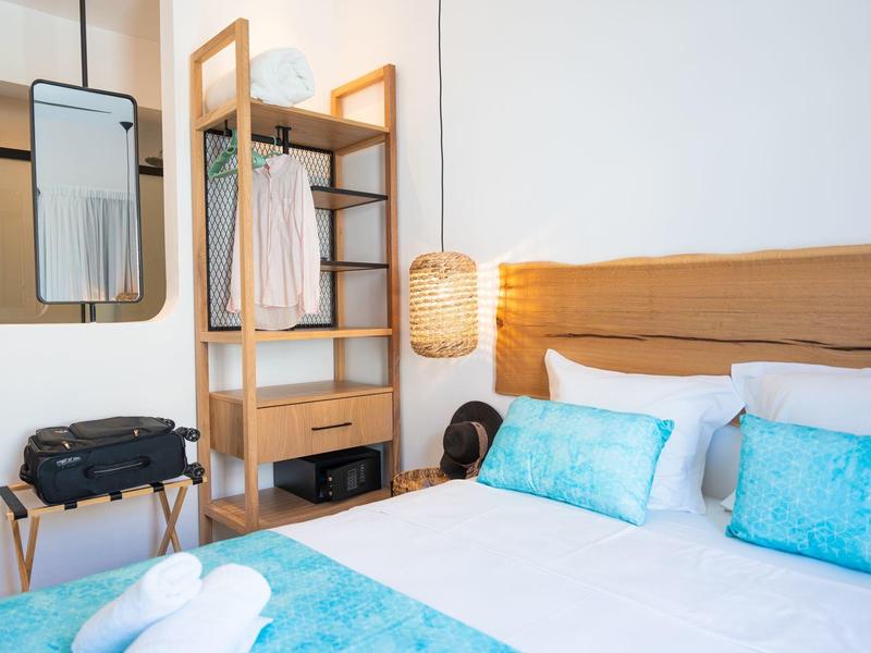 Lichte hotelkamer met tweepersoonsbed, houten plank, open kledingkasten, lichte inrichting en koffer.