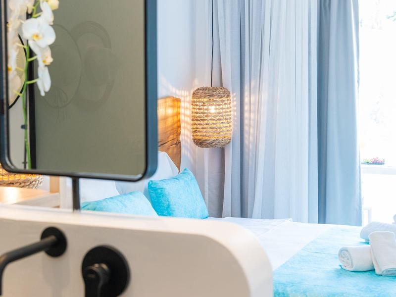 Lichte hotelkamer met blauwe beddengoed, moderne wastafel en hanglamp.