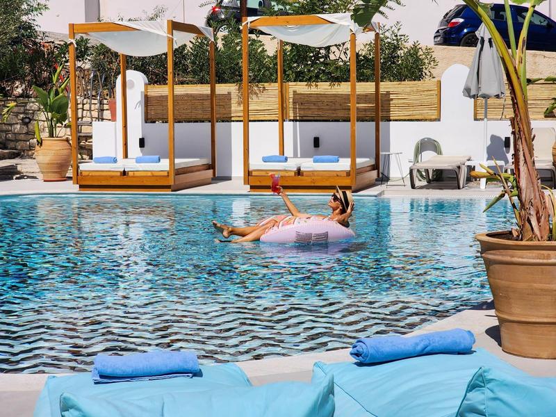 Persoon ontspant op een roze opblaasring in het heldere zwembad van een resort met zonneschermen.