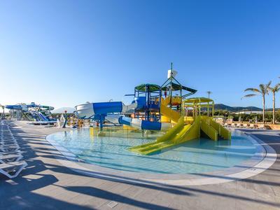 Moderner Wasserpark mit Rutschen, flachem Pool, Sonnendeck und Palmen unter blauem Himmel.