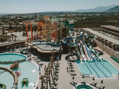 Freizeitpark mit Wasserrutschen, Schwimmbecken, Kletterwand und vielen Besuchern an einem sonnigen Tag.
