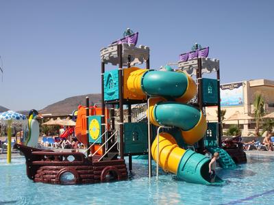 Aire de jeux aquatique colorée avec toboggans et décoration de navire dans une piscine sous un ciel clair.