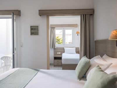 Hell und schlicht eingerichtetes Schlafzimmer mit Betten, Kissen und Blick durch Tür zum weiteren Zimmer.