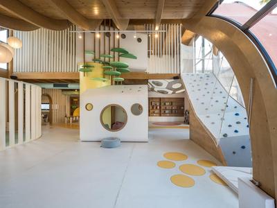 Salle de jeux moderne et lumineuse avec arbre artificiel et mur d'escalade en bois.