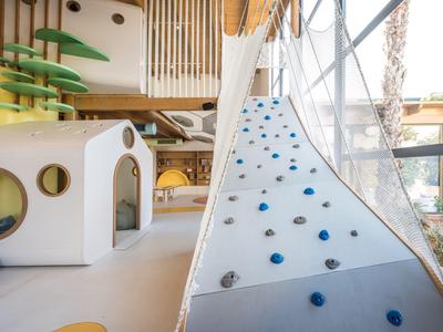 Innenbereich mit Kletterwand, Spielhäusern und bunten Spielstrukturen aus Holz und Kunststoff.