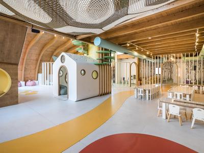 Jardin d'enfants lumineux et moderne avec des structures de jeu en bois et des petites tables sous un plafond en bois.