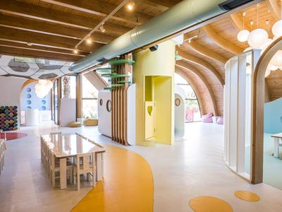 Heller, moderner Kindergartenraum mit bunten Böden, Holzmöbeln und geschwungenen Deckenformen.