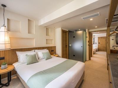 Modernes Hotelzimmer mit großem Bett, weißen Wänden, Holzdekor und gläserner Badtür.