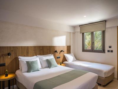 Modernes Schlafzimmer mit Holzpaneel, Doppel- und Einzelbett, hellen Kissen und dekorativem Tisch.