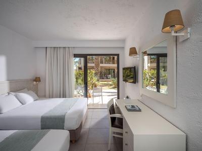 Chambre d'hôtel lumineuse avec deux lits, bureau et vue sur le jardin.
