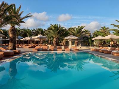 Une piscine claire entourée de chaises longues et de palmiers sous un ciel bleu dans un hôtel.