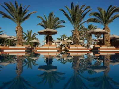 Chaises longues et parasols près d'une piscine avec des palmiers sous un ciel clair.
