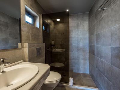 Salle de bain d'hôtel moderne avec douche à l'italienne, carrelage gris et grands miroirs.