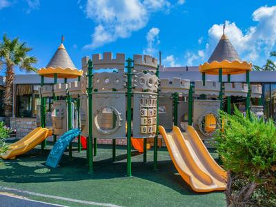 Aire de jeux colorée avec toboggans et structure de château sous un ciel bleu dans un hôtel.