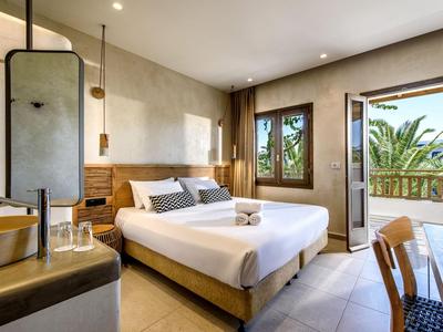 Chambre d'hôtel moderne avec lit double, accents en bois et balcon donnant sur des palmiers.