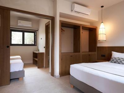 Chambre d'hôtel moderne avec deux lits simples, armoire en bois et éclairage chaleureux.