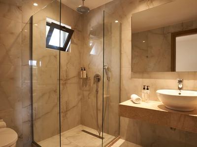 Salle de bain moderne avec douche en verre, murs en marbre, et lavabo rond sur étagère en bois.
