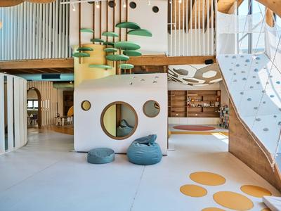 Espace de jeu moderne d'hôtel avec fenêtres rondes, pouf bleu et escalier en bois.