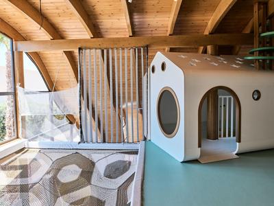 Espace de jeu confortable dans un hôtel avec poutres en bois et maisonnette moderne pour enfants.