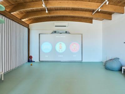 Salle vide avec sol vert, plafond en bois et écran sur le mur.