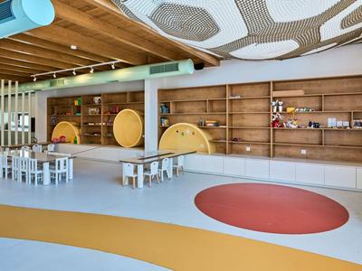 Hall moderne et lumineuse avec des éléments en bois, des espaces assis et des tapis colorés décoratifs.