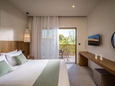 Chambre d'hôtel lumineuse avec grand lit, accents en bois et balcon donnant sur la verdure.