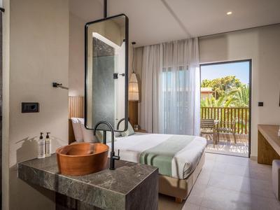 Chambre d'hôtel moderne avec lit, baignoire et balcon donnant sur la verdure.