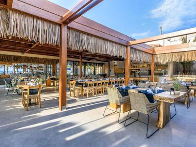Restaurant ouvert avec toit en bois et paille dans une station de vacances ensoleillée.