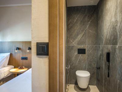 Chambre d'hôtel moderne avec un lit clair et une salle de bain attenante avec des carreaux gris.