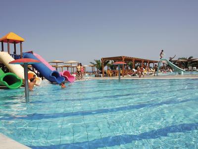 Großer Pool mit Wasserrutschen, sonnigem Himmel und Liegestühlen im Hintergrund.