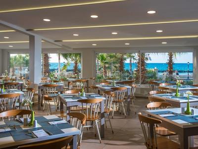 Großer, moderner Speisesaal mit Holztischen, Stühlen und Blick auf den Außenbereich mit Bäumen.