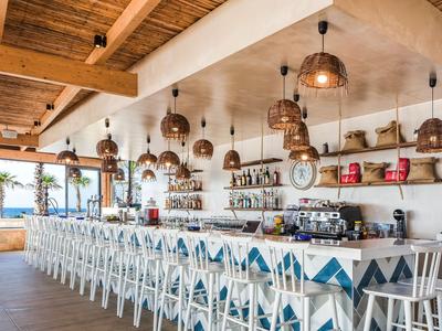 Bar lumineuse avec chaises bleues et blanches, lampes suspendues et poutres en bois.