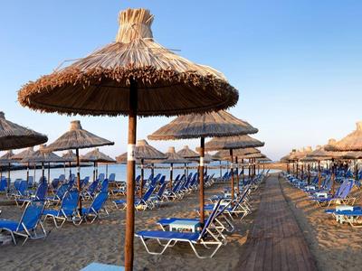 Strand mit vielen blauen Liegestühlen und Strohschirmen unter klarem, blauem Himmel.